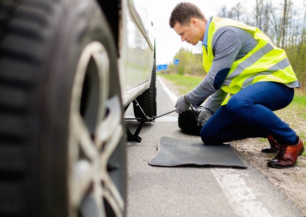 Man changing a flat tire on the side of the road